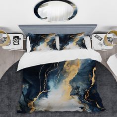 a bed with a blue and gold comforter set on top of it, next to a mirror