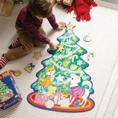 a little boy that is kneeling down on the floor with a christmas tree shaped rug