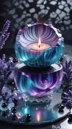 a blue and purple candle sitting on top of a glass bowl next to some flowers