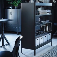 a black bookcase with white bins is in the middle of a room next to a table and chairs