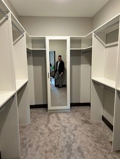 a man standing in front of a mirror in a walk - in closet with white shelving