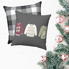 two pillows with sweaters on them next to christmas ornaments and a fir tree in the background