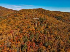 a cross on top of a hill surrounded by trees in the fall colors with blue sky