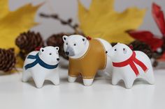 three small white polar bears standing next to each other in front of autumn leaves and pine cones