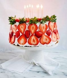 a strawberry cake with white frosting and strawberries on top, surrounded by candles