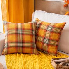 two yellow plaid pillows sitting on top of a bed next to a basket with an orange flower