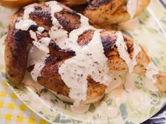 some chicken is sitting on a plate with white sauce and garnished potatoes in the background