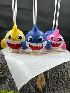 three toothbrushes shaped like shark heads on top of a white cloth covered tree stump