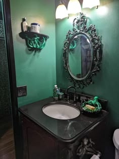 a bathroom with green walls and black counter top, mirror above the sink and toilet