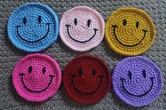 four crocheted coasters with smiley faces on them, all in different colors