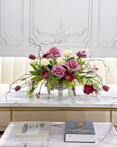 a marble table topped with a vase filled with pink and white flowers next to two books