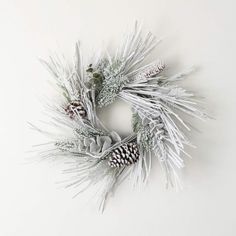 a white wreath with pine cones and evergreen needles on the front, hanging from a wall