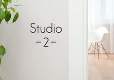 a white wall with the words studio 2 = 2 on it next to a green plant