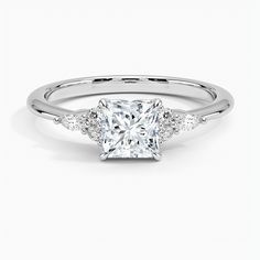 a cushion cut diamond ring with two side stones on the band and an accent set in white gold