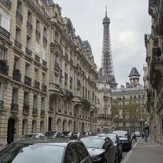 cars are parked on the sidewalk in front of tall buildings with eiffel tower in the background