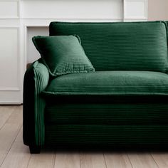 a green couch sitting on top of a hard wood floor next to a white fireplace