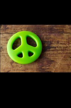 a green plastic peace sign sitting on top of a wooden table next to a bottle opener