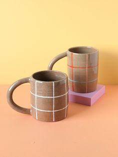 two coffee mugs sitting next to each other on top of a pink and yellow table