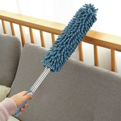 a person holding a blue dust mop on top of a couch