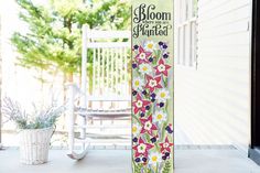 a wooden sign sitting on top of a porch next to a white chair and potted plant