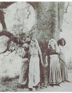 an old photo of three women standing next to a large tree in the grass and dirt