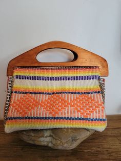 an orange and white purse sitting on top of a wooden stand next to a rock