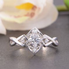 a diamond ring sitting on top of a table next to a white flower with petals in the background