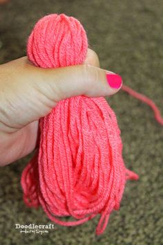 a ball of pink yarn being held by a woman's hand with red nail polish