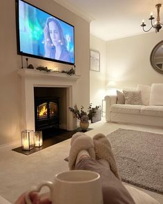 a person holding a coffee cup in front of a fireplace with a flat screen tv above it