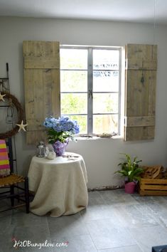 there is a table with flowers on it in front of the window and two wooden shutters