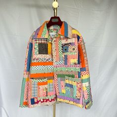 a multicolored patchwork jacket hanging on a wooden stand against a white backdrop