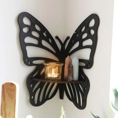 a candle is lit on a shelf with a butterfly shaped wall mounted decoration above it