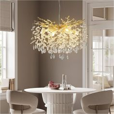 a chandelier hanging over a white table in a room with beige walls and chairs