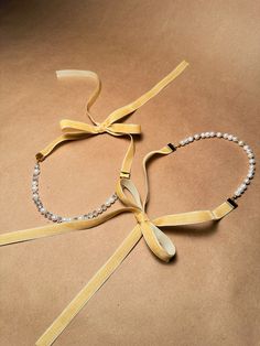 two pieces of yellow ribbon tied to each other on a brown surface with white beads