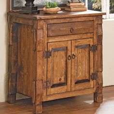 a wooden cabinet with two doors and drawers in front of a window that has a potted plant on top of it