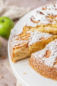 a white plate topped with cake covered in powdered sugar next to an green apple