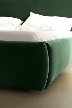 a green bed with white sheets and pillows on it's headboard is shown