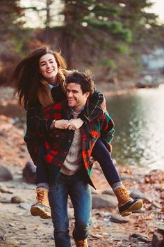 a man carrying a woman on his back while walking along a river bank in the woods