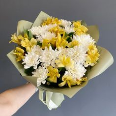 a bouquet of yellow and white flowers being held by a person's right hand