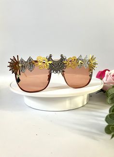 💛Unisex rose gold statement sunglasses by Alexis Exclusive. 💛These unique glasses will add that special touch to your summer / festival / holiday outfits... Be the one and only person in this unique design. 💛The frames are oversized and they have tinted rose gold/orange lenses. All along the top they have been designed in a mixture of funky jewels, embellishments and trinkets. 💛A medium weight design that are comfortable to wear. 💛Great for festivals, weddings, holidays, burning man or everyday wear to add some glam to your outfits.  💛Light UV protection. 💛Exclusive design made by myself, you won't see any others like these anywhere else. 💛All my glasses come in a black branded pouch to keep them safe, please also handle with care. 💛Checkout the full collection of Sunnies here : Bohemian Sunglasses With Uv Protection For Vacation, Summer Metal Sunglasses With Mirrored Lenses, Summer Party Sunglasses With Metal Frame, Metal Sunglasses With Mirrored Lenses For Summer, Summer Mirrored Metal Sunglasses, Metal Sunglasses With Gradient Lenses For Beach, Summer Shield Sunglasses With Mirrored Glass Lenses, Metal Sunglasses With Gradient Lenses For The Beach, Spring Party Sunglasses With Metal Frame