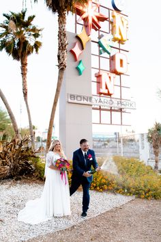 Catch this joyful moment at a unique venue with a neon "The Boneyard Park" sign backdrop! The groom pops champagne 🍾, perfectly capturing the bubbly spray, while the bride beams in her timeless long sleeve wedding dress 💍. A rich wildflower bouquet and navy suit complete the scene amidst palm trees and golden-hour sunlight. Save for unique wedding ideas and a wildflower wedding theme! 🌸💒 #weddingideas #unquieweddingideas #longsleeveweddingdress #wildflowerweddingtheme #weddings Four Seasons Las Vegas, Las Vegas Boulevard, Pop Champagne