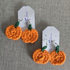 two orange crocheted pumpkin earrings with green leaves on each earring and tag attached to them