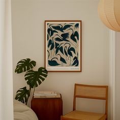 a chair sitting next to a plant in a living room under a framed art piece