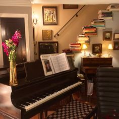 a piano in a living room next to a stair case with books on it and a vase filled with flowers