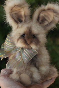 a person holding a small teddy bear in their hand with a bow on it's head