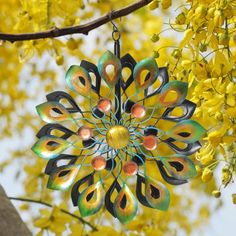 a metal ornament hanging from a tree branch with yellow flowers in the background