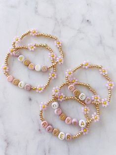 four bracelets with letters and flowers on them sitting on a marble counter top next to each other