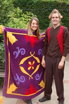 two people standing next to each other holding a purple and yellow blanket