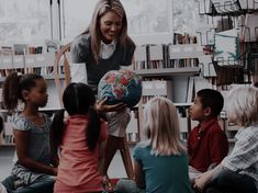 there is a woman holding a globe in front of children sitting on the floor and looking at it