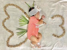 a baby laying on top of a white sheet next to a palm leaf and rope